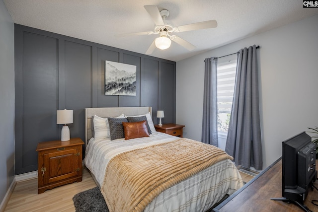 bedroom featuring light wood-type flooring, a textured ceiling, ceiling fan, and a decorative wall