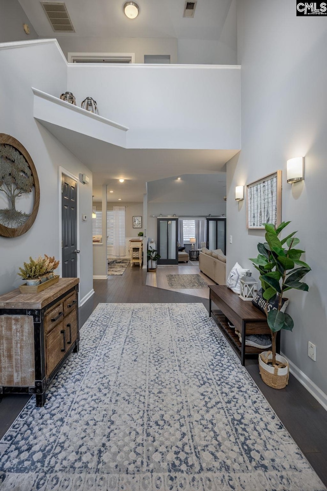 corridor with visible vents, baseboards, a towering ceiling, and wood finished floors