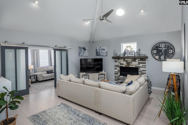 living area with a ceiling fan, baseboards, lofted ceiling with beams, a fireplace, and light wood-type flooring