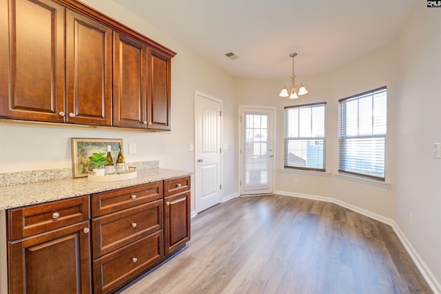 kitchen featuring light stone counters, wood finished floors, baseboards, an inviting chandelier, and decorative light fixtures