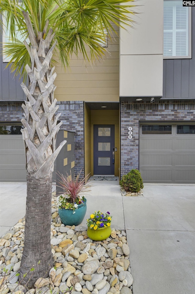 doorway to property featuring an attached garage, brick siding, and driveway