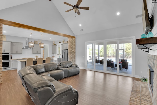 living area with visible vents, high vaulted ceiling, light wood-style flooring, a fireplace, and ceiling fan