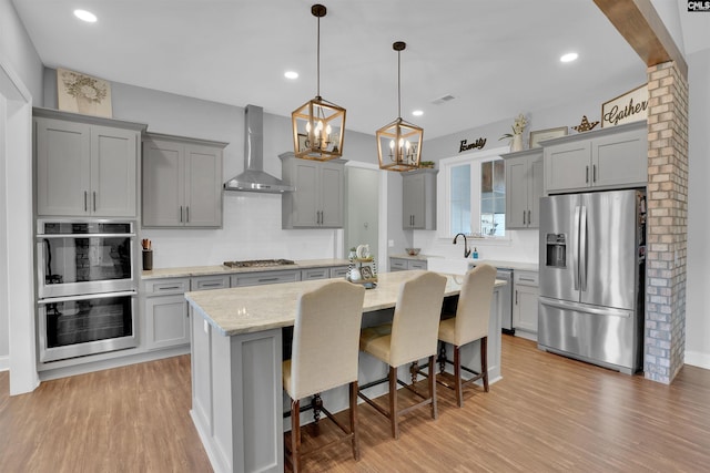 kitchen featuring wall chimney range hood, gray cabinets, and stainless steel appliances