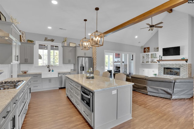 kitchen featuring beamed ceiling, ceiling fan with notable chandelier, a sink, stainless steel appliances, and a fireplace