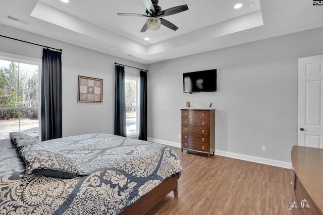 bedroom featuring visible vents, a raised ceiling, baseboards, and wood finished floors