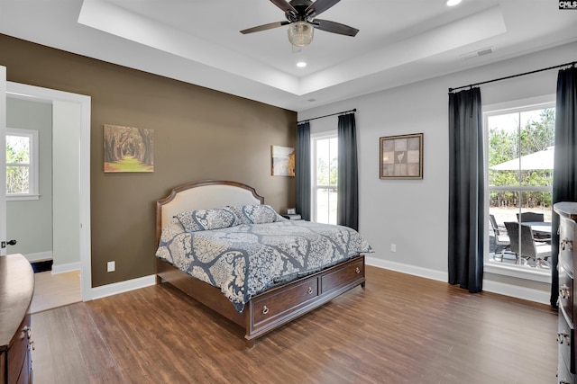 bedroom with visible vents, a tray ceiling, wood finished floors, recessed lighting, and baseboards