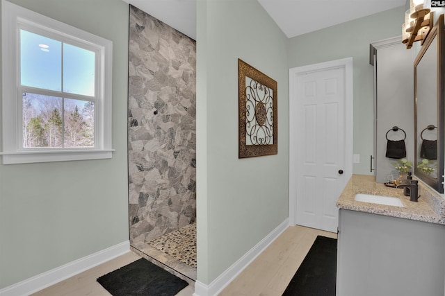 bathroom featuring wood finished floors, tiled shower, baseboards, and a sink