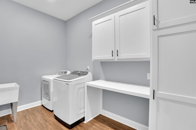 clothes washing area with washer and clothes dryer, cabinet space, baseboards, and wood finished floors