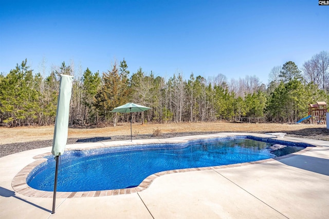 outdoor pool featuring a forest view, a patio area, and a playground