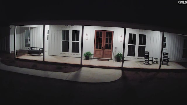 exterior entry at twilight with board and batten siding, french doors, and covered porch