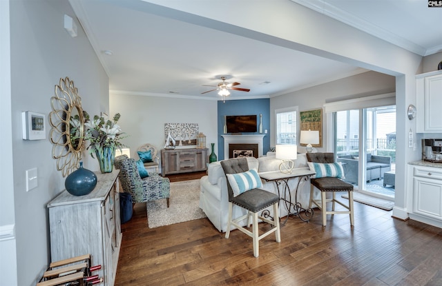 living area with a fireplace, ceiling fan, dark wood-style flooring, and ornamental molding