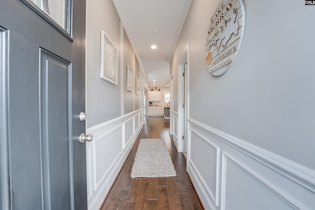 hallway with dark wood-type flooring, a decorative wall, and wainscoting