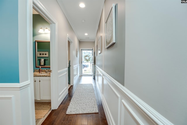 corridor with crown molding, a wainscoted wall, dark wood-style floors, a decorative wall, and a sink