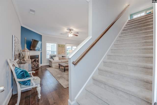 staircase featuring visible vents, ornamental molding, a ceiling fan, wood finished floors, and a fireplace