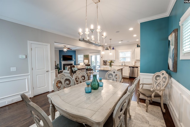 dining room with dark wood finished floors, recessed lighting, wainscoting, crown molding, and ceiling fan with notable chandelier