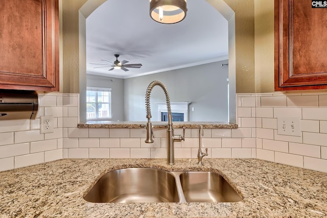 details with brown cabinets, a ceiling fan, a sink, crown molding, and light stone countertops