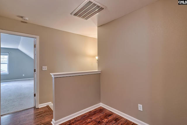 empty room featuring visible vents, baseboards, dark wood finished floors, and vaulted ceiling