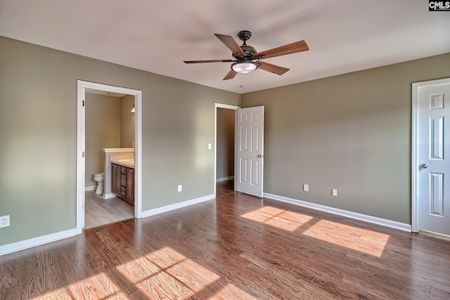 unfurnished bedroom featuring baseboards, ensuite bath, wood finished floors, and a ceiling fan