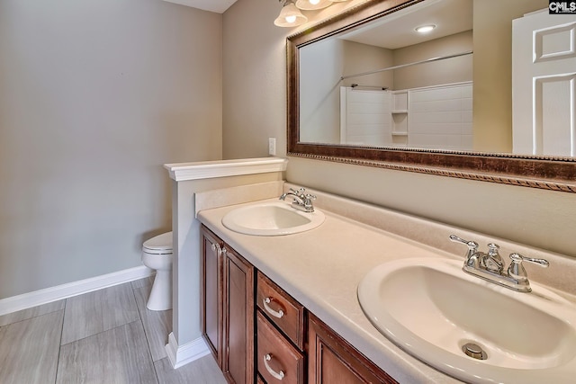 bathroom featuring double vanity, toilet, baseboards, and a sink