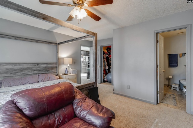 carpeted bedroom with baseboards, ensuite bath, a closet, a textured ceiling, and a walk in closet