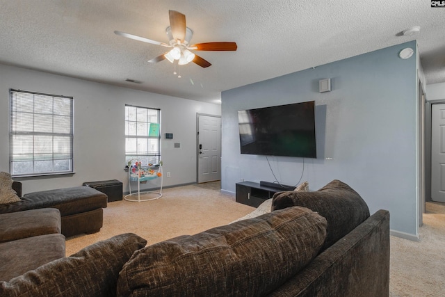 living room featuring visible vents, light carpet, a textured ceiling, baseboards, and ceiling fan