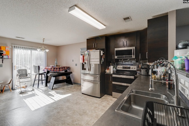 kitchen featuring visible vents, an inviting chandelier, stainless steel appliances, dark brown cabinetry, and dark countertops