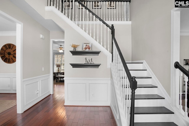 stairs with crown molding, hardwood / wood-style floors, a high ceiling, a decorative wall, and a ceiling fan