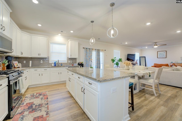 kitchen with stainless steel microwave, a kitchen island, open floor plan, gas range, and light wood-type flooring