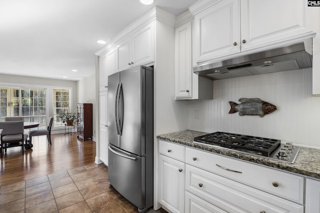 kitchen with under cabinet range hood, appliances with stainless steel finishes, white cabinets, and dark stone countertops