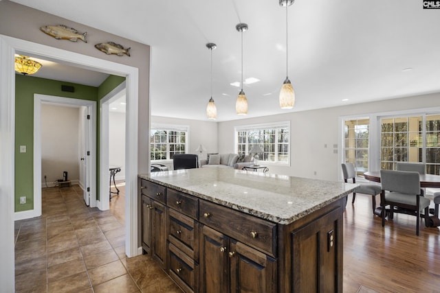 kitchen featuring pendant lighting, open floor plan, a center island, light stone countertops, and dark brown cabinets