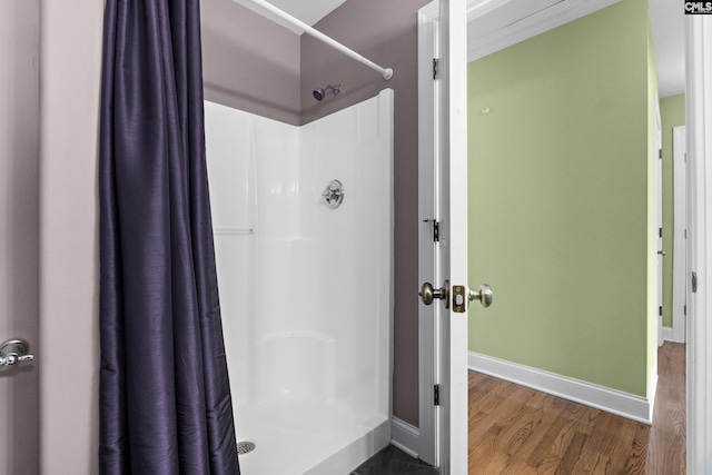 bathroom with baseboards, wood finished floors, and a shower stall