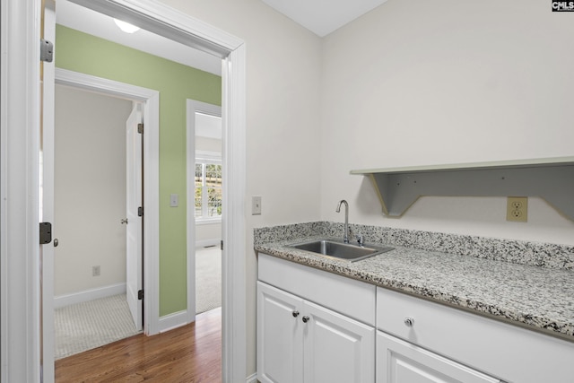 kitchen featuring a sink, white cabinetry, baseboards, dark wood-style flooring, and light stone countertops