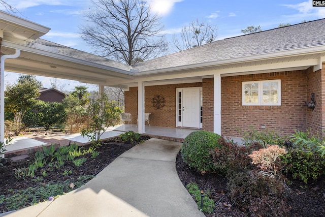 property entrance with a porch, brick siding, and roof with shingles