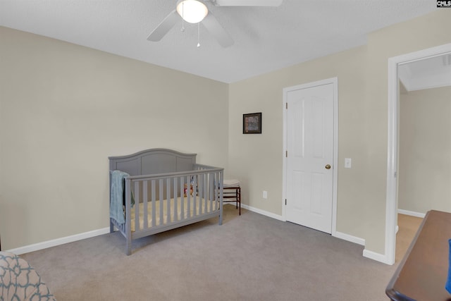 bedroom with a ceiling fan, a crib, carpet, and baseboards