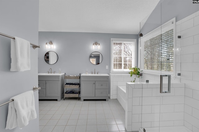 bathroom featuring two vanities, a sink, a textured ceiling, tile patterned flooring, and a bath