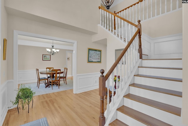 stairs featuring an inviting chandelier, a decorative wall, wood finished floors, and wainscoting