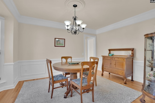 dining area featuring wainscoting, crown molding, light wood-style floors, and an inviting chandelier