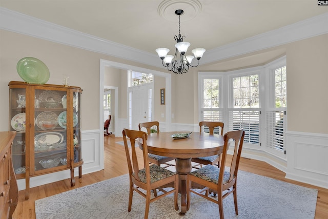 dining area with a chandelier, wainscoting, light wood finished floors, and crown molding