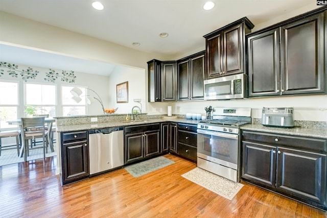 kitchen featuring light wood finished floors, recessed lighting, a peninsula, stainless steel appliances, and a sink