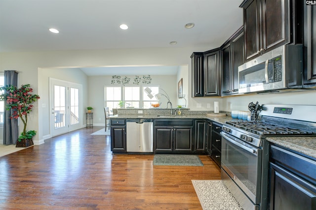 kitchen featuring a sink, wood finished floors, recessed lighting, stainless steel appliances, and a peninsula