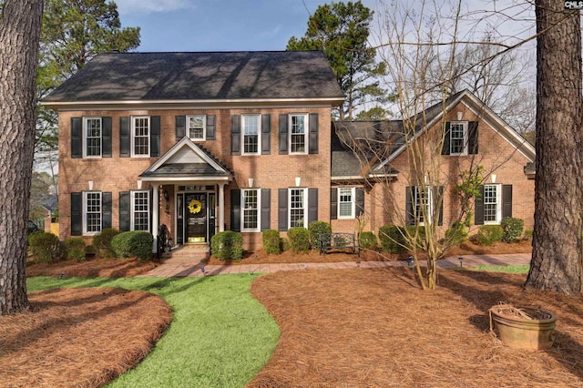 colonial house featuring brick siding, roof with shingles, and a front lawn