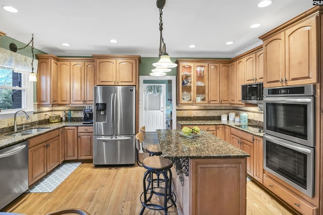 kitchen with backsplash, dark stone counters, light wood-style floors, stainless steel appliances, and a sink