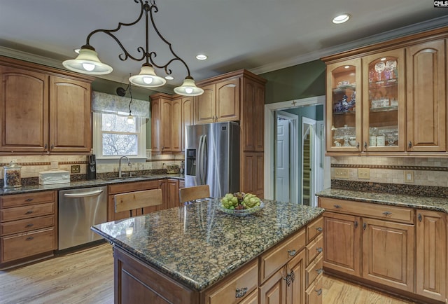 kitchen featuring ornamental molding, a sink, a center island, stainless steel appliances, and glass insert cabinets