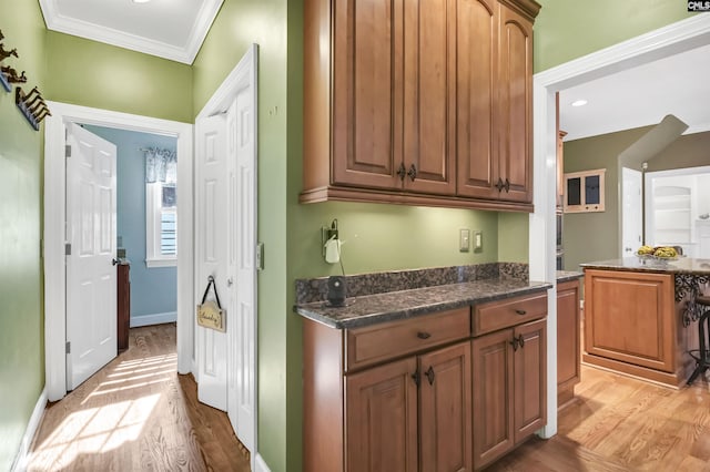 kitchen with dark stone counters, light wood-style flooring, baseboards, and ornamental molding