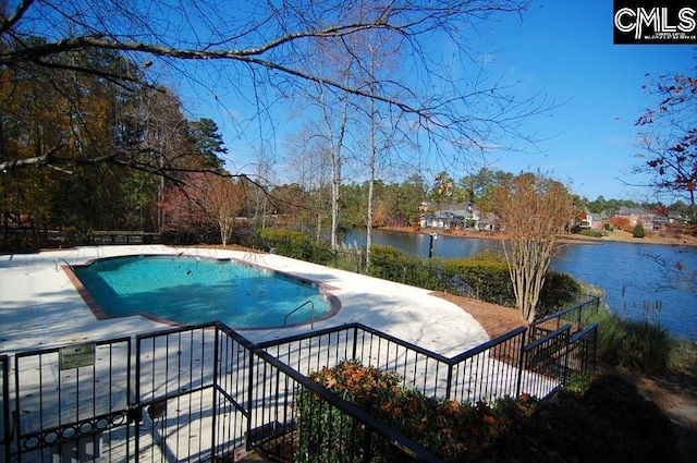 outdoor pool with a patio area, fence, and a water view