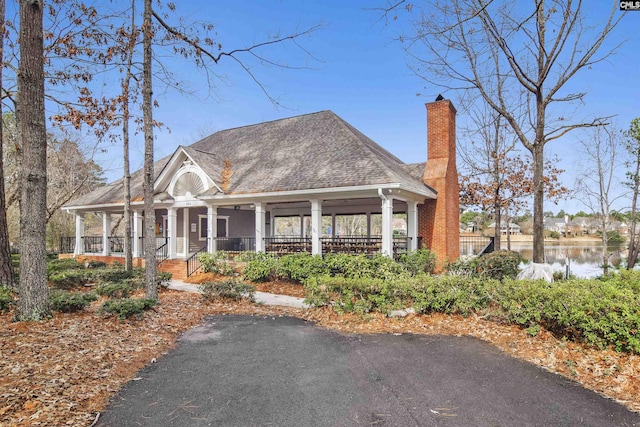 view of front of property featuring covered porch, a chimney, a water view, and a shingled roof