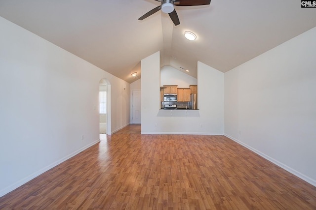 unfurnished living room featuring a ceiling fan, wood finished floors, arched walkways, baseboards, and vaulted ceiling