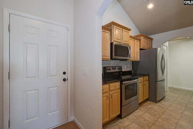 kitchen featuring lofted ceiling, arched walkways, stainless steel appliances, dark countertops, and backsplash