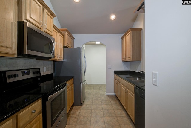 kitchen with a sink, arched walkways, appliances with stainless steel finishes, decorative backsplash, and baseboards