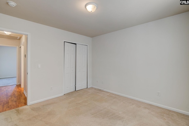 unfurnished bedroom with light carpet, a closet, attic access, and baseboards